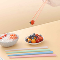 Chopsticks in use picking cherry tomato, with colorful set on table, ideal for hygienic family dining and food handling.