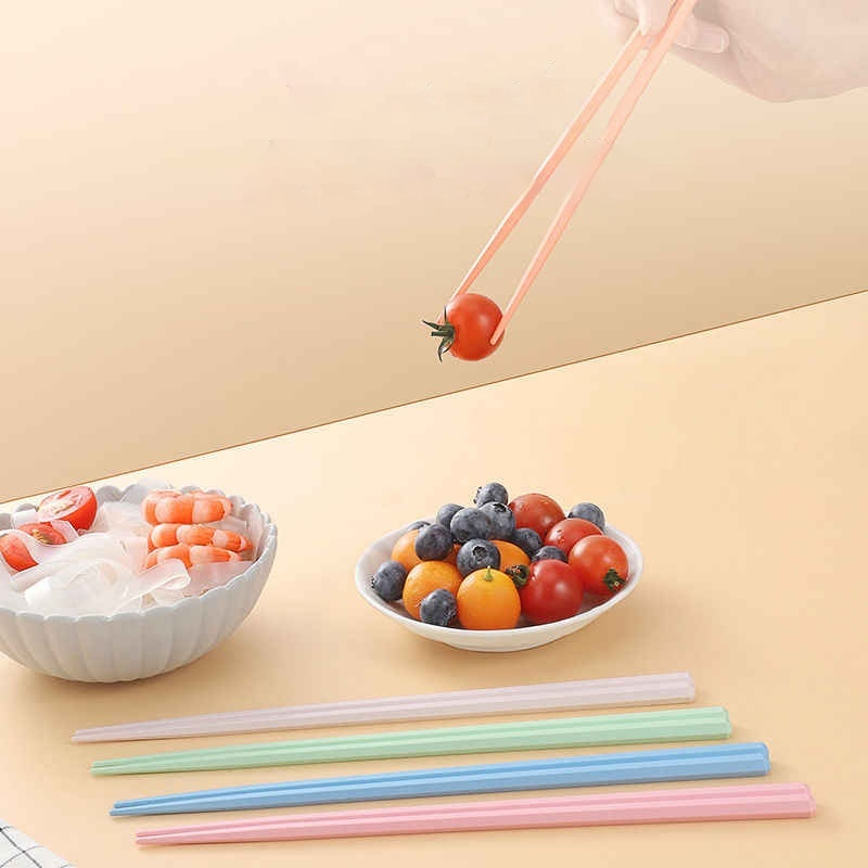 Chopsticks in use picking cherry tomato, with colorful set on table, ideal for hygienic family dining and food handling.
