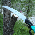 Zhang Xiaoquan 235mm pruning handsaw cutting thick tree branch. Sharp 65Mn steel blade ensures clean and fast cuts.