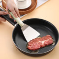 Steel spatula flipping steak in a frying pan, demonstrating its strength and precision for cooking tasks in the kitchen.
