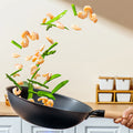 Coating-free iron wok from Zhang Xiaoquan AU tossing shrimp and vegetables mid-air, perfect for healthy high-heat stir-frying.
