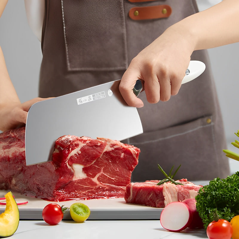 The Chef's Cutting & Sharpening Kit featuring a 305mm cleaver slicing through raw meat on a cutting board, surrounded by fresh vegetables.