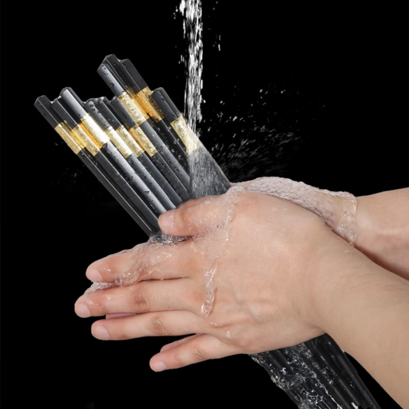 Black chopsticks with golden accents being washed under running water.