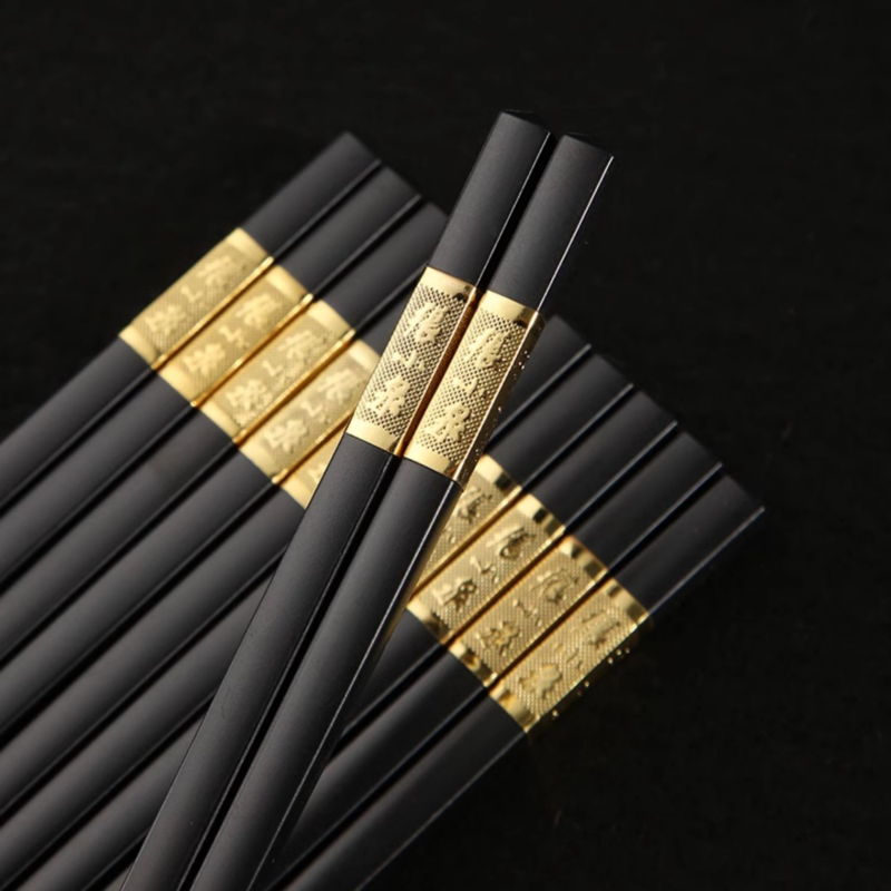 Close-up of black chopsticks with intricate golden patterns on the handles.