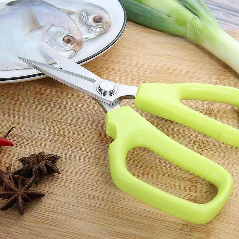 Multi-purpose kitchen scissors cutting fish and vegetables on a wooden board.