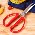 Red-handled stainless steel scissors placed on a crafting table with fabric and thread.