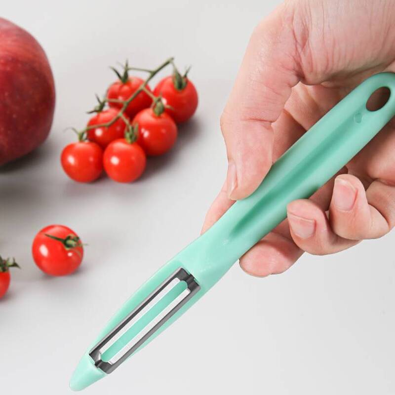 Hand holding mint green peeler near fresh tomatoes and apple.