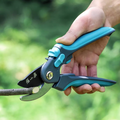 Hand holding SK5 pruning shears cutting a branch outdoors.