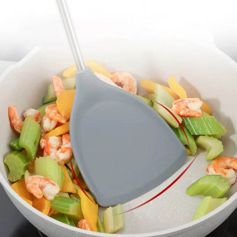 Silicone spatula stirring vegetables and shrimp in a pan.