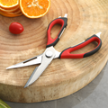 Kitchen scissors on a wooden board with sliced oranges and a cherry tomato.