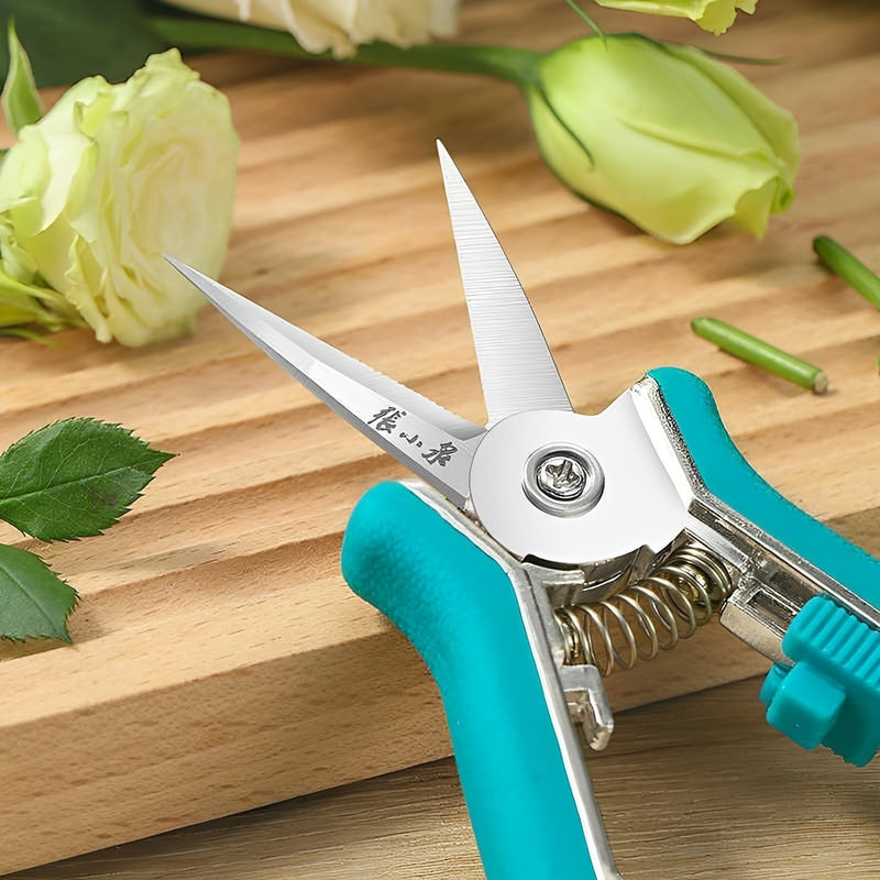 Pruning scissors cutting white rose stems on a wooden surface.