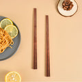 Two ironwood chopsticks placed on a beige surface with food and decor.