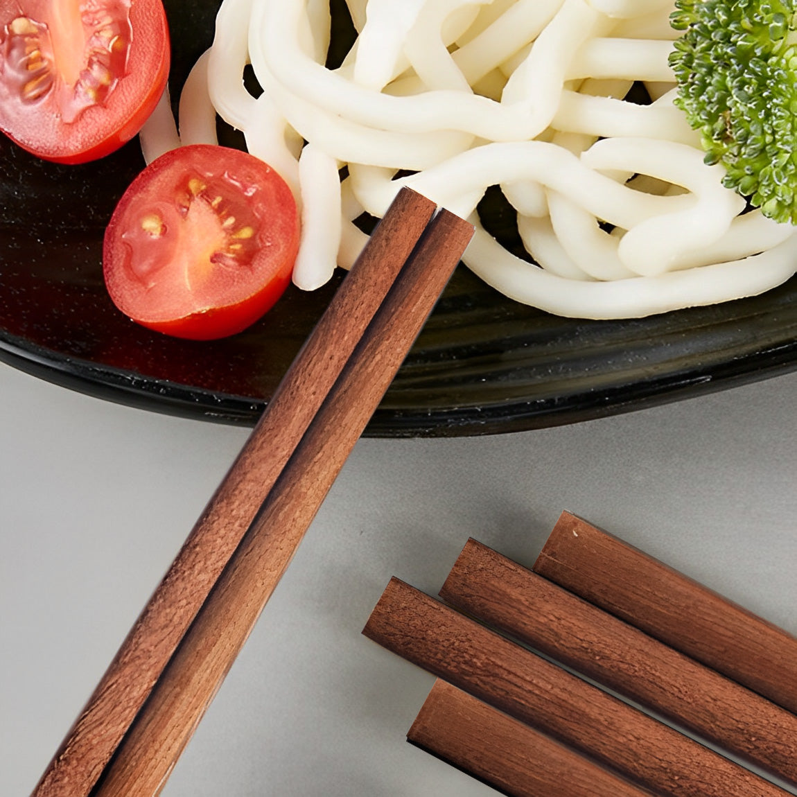 Close-up of ironwood chopsticks holding noodles with vegetables.