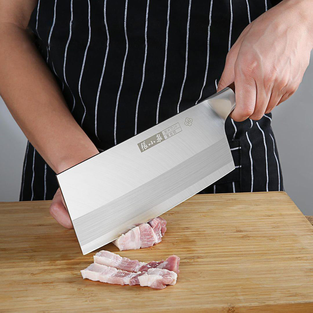 Chinese cleaver in use, slicing meat on a wooden cutting board with precision.