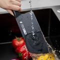 Chinese cleaver being rinsed under water with fresh vegetables nearby.