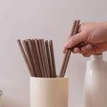 Hand picking a pair of sandalwood chopsticks from a holder on a minimalist table.