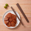 Sandalwood chopsticks placed beside a plate of lotus root slices on a wooden table.